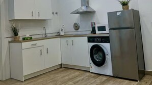 Une cuisine moderne avec des armoires blanches, une hotte de cuisinière en acier inoxydable, un lave-linge encastré et un réfrigérateur.