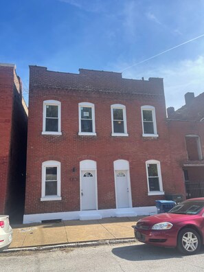 A red brick building with white-framed windows and doors, a visible address sign, and a parked car in front. - Experience the Charm of Hyde Park in this Renovated St. Louis Retreat (St. Louis)