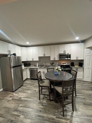 A modern kitchen with white cabinets, stainless steel appliances, and a dining area with a round table and chairs. - Experience the Charm of Hyde Park in this Renovated St. Louis Retreat (St. Louis)