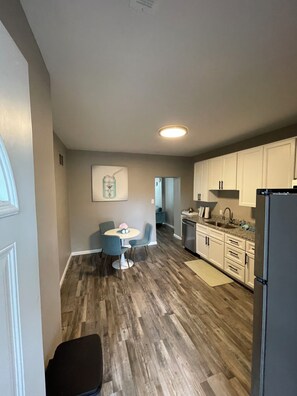 A modern kitchen with white cabinets, a dining area with a round table and chairs, and a wooden floor. - Experience the Charm of Hyde Park in this Renovated St. Louis Retreat (St. Louis)