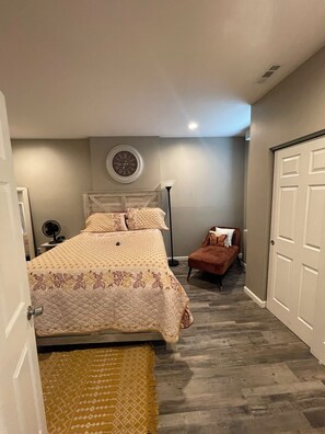 Une chambre à coucher avec un lit, une chaise, une horloge au mur et une porte.