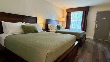 Une chambre d’hôtel avec deux lits, une tête de lit en bois, une table de chevet, une lampe, une fenêtre avec des rideaux et une porte.