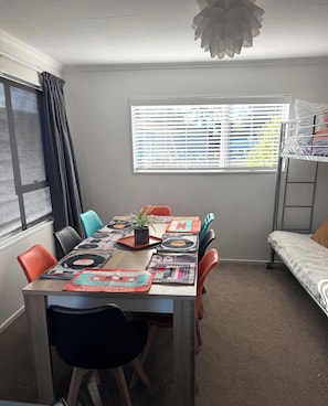 A dining area with a table set for six, a bunk bed, and a window with blinds.