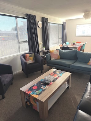 A living room with a sofa, armchairs, a coffee table with vinyl records, a dining table with chairs, and a potted plant.
