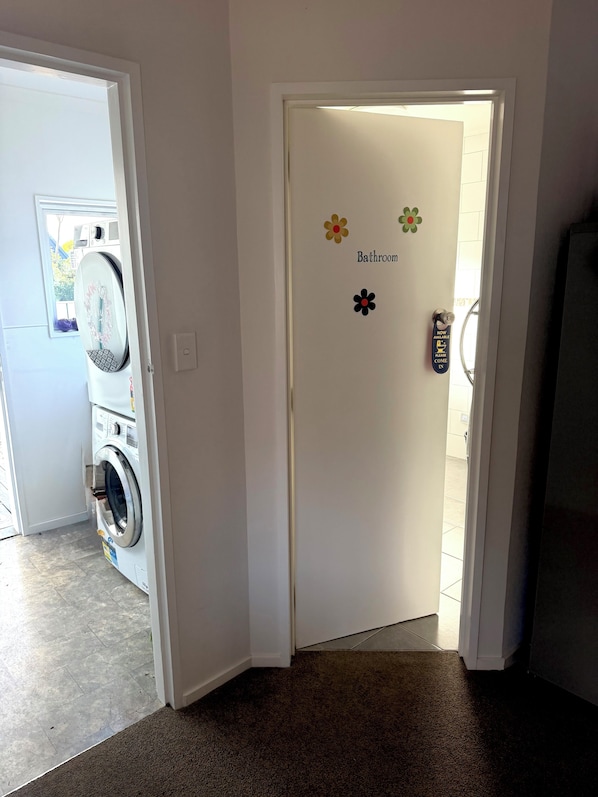 A bathroom door with a sign indicating it's now available, a washing machine, and a door with a flower decal.
