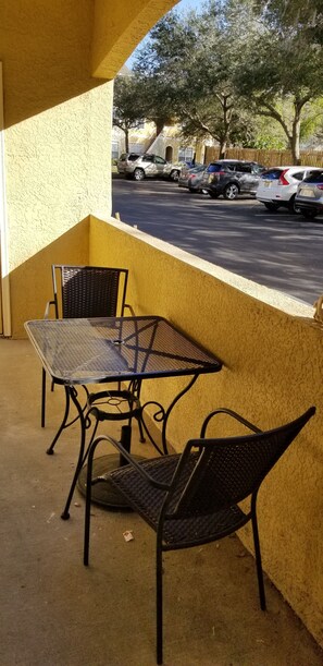 Eine Terrasse mit einem Metalltisch und zwei Stühlen mit Blick auf einen Parkplatz mit mehreren Autos.