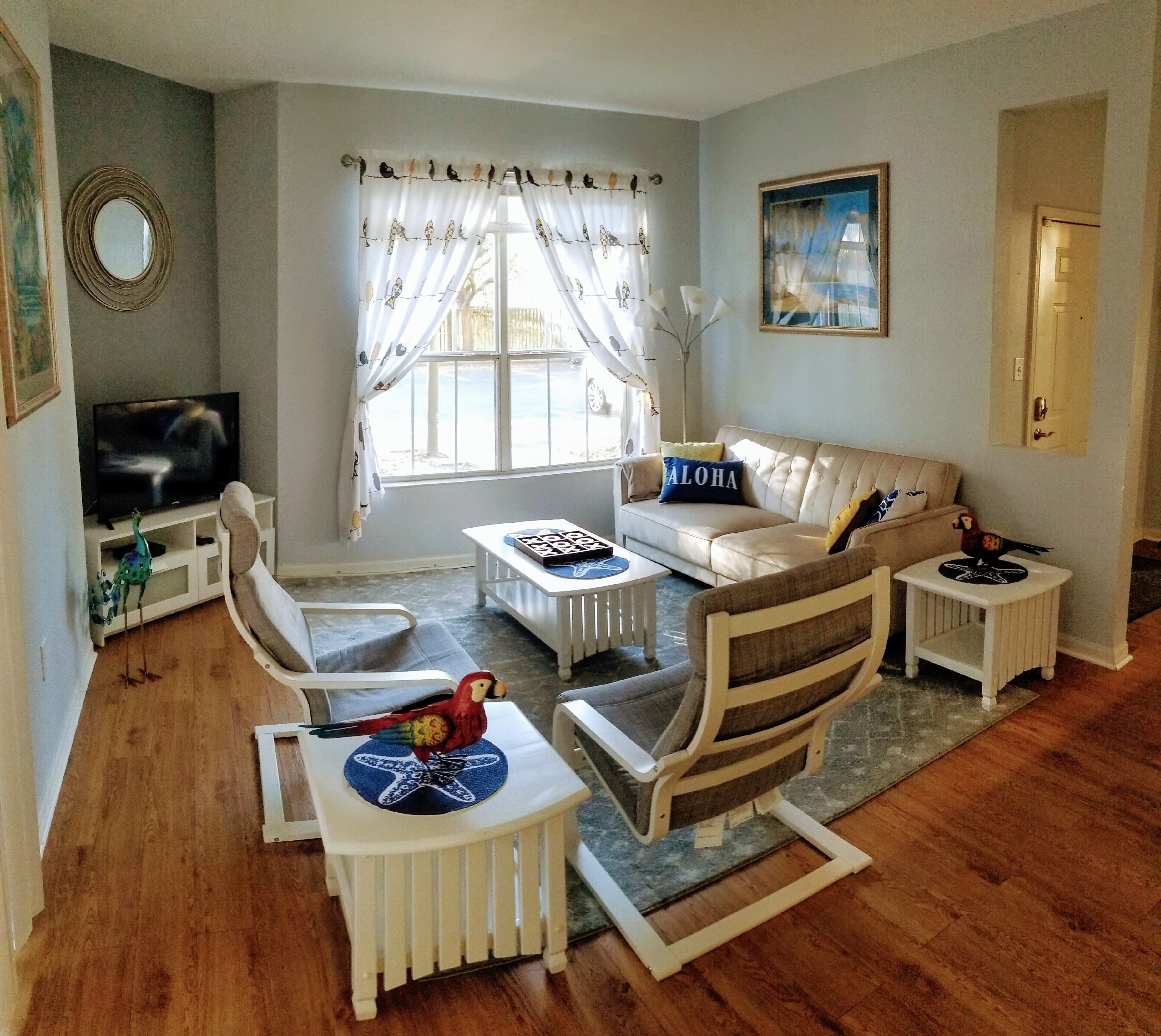 A living room with a sofa, chairs, a coffee table, a TV, and a window with curtains.