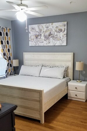A bedroom with a bed, nightstands, a ceiling fan, a wall-mounted artwork, and a window with curtains. - Bright and Spacious 1Bed/1Bath condo. (Clearwater)