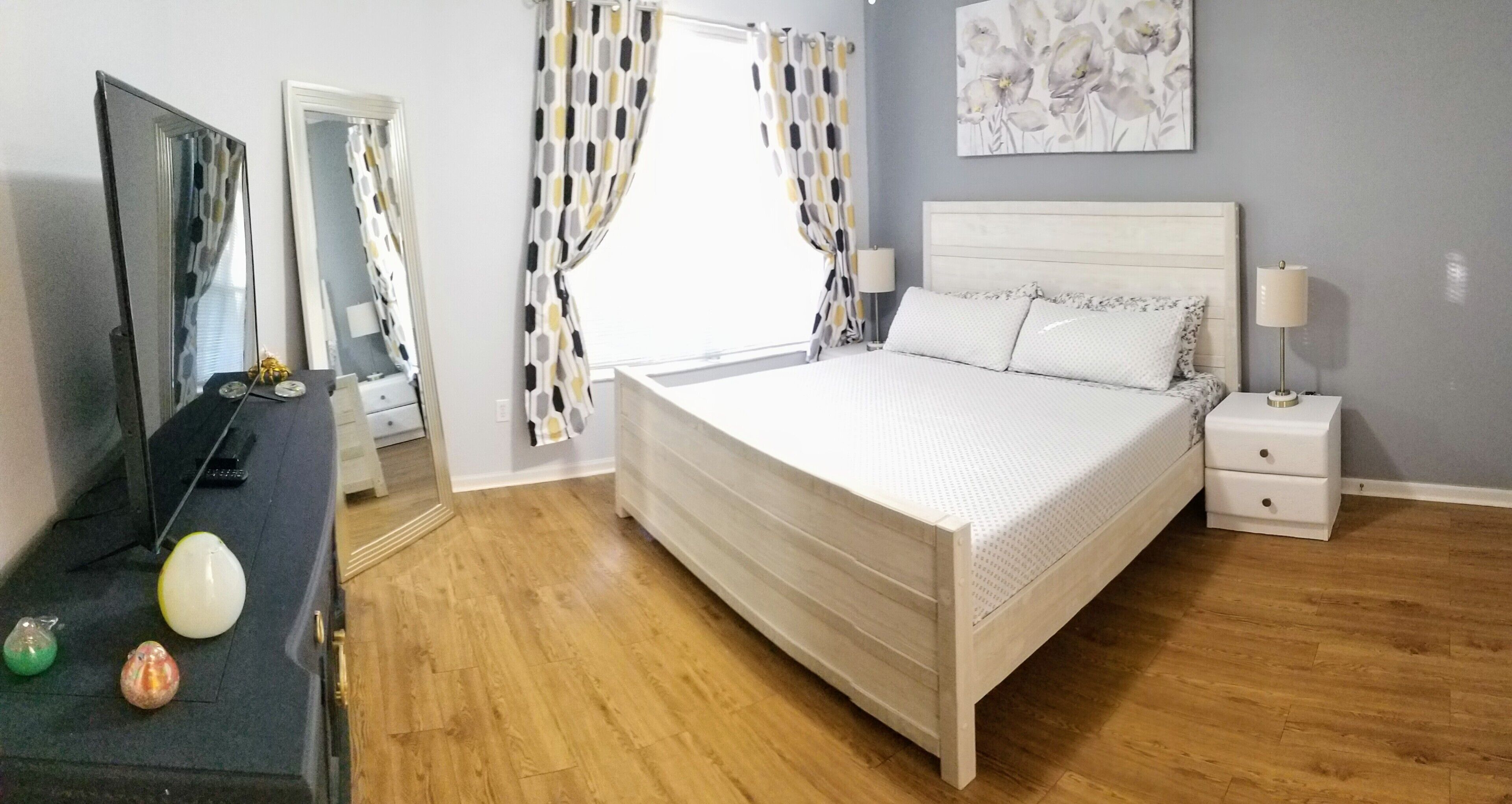 Een slaapkamer met een bed, nachtkastjes, een kaptafel, een spiegel en een raam met gordijnen.