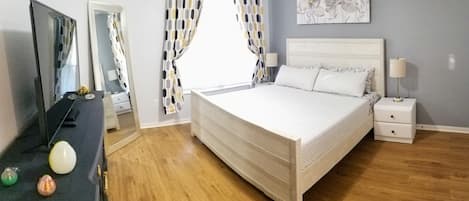 A bedroom with a bed, bedside tables, a dresser, a mirror, and a window with curtains.