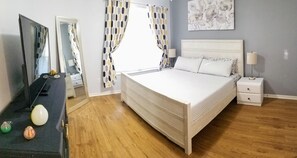 Une chambre à coucher avec un lit, des tables de chevet, une commode, un miroir et une fenêtre avec des rideaux.