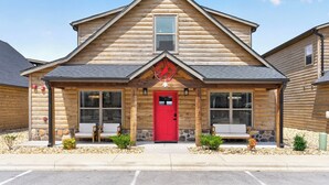 A log cabin with a red door, two windows on the front, a small porch, and a stone foundation. - Luxe 4BR-4BA, Branson Retreat with Lake Views, Pools + Pickleball (Branson)