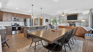 A modern kitchen with stainless steel appliances, a dining area with a wooden table and chairs, and a fireplace. - Luxe 4BR-4BA, Branson Retreat with Lake Views, Pools + Pickleball (Branson)
