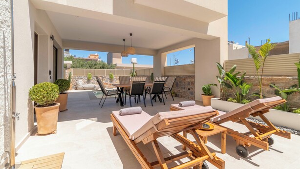 Eine Terrasse im Freien mit Liegestühlen, einem Tisch und Blumentöpfen.