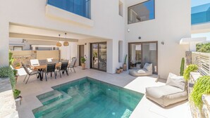 Ein modernes Haus mit Swimmingpool, Sitzgelegenheiten im Freien und einer Terrassenfläche.