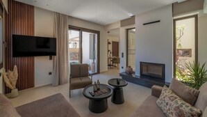 Ein modernes Wohnzimmer mit Fernseher, Kamin und Essbereich, der durch eine Glastür sichtbar ist.