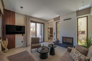 A modern living room with a flat-screen TV, a fireplace, and a dining area visible through a glass door. - Villa Penelope, Heraklion, Crete, Gazi (Gazi)