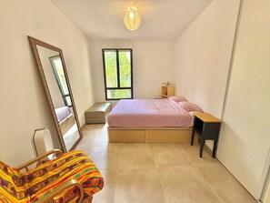 Ein Schlafzimmer mit Bett, Nachttisch, Stuhl, Fenster und Spiegel.