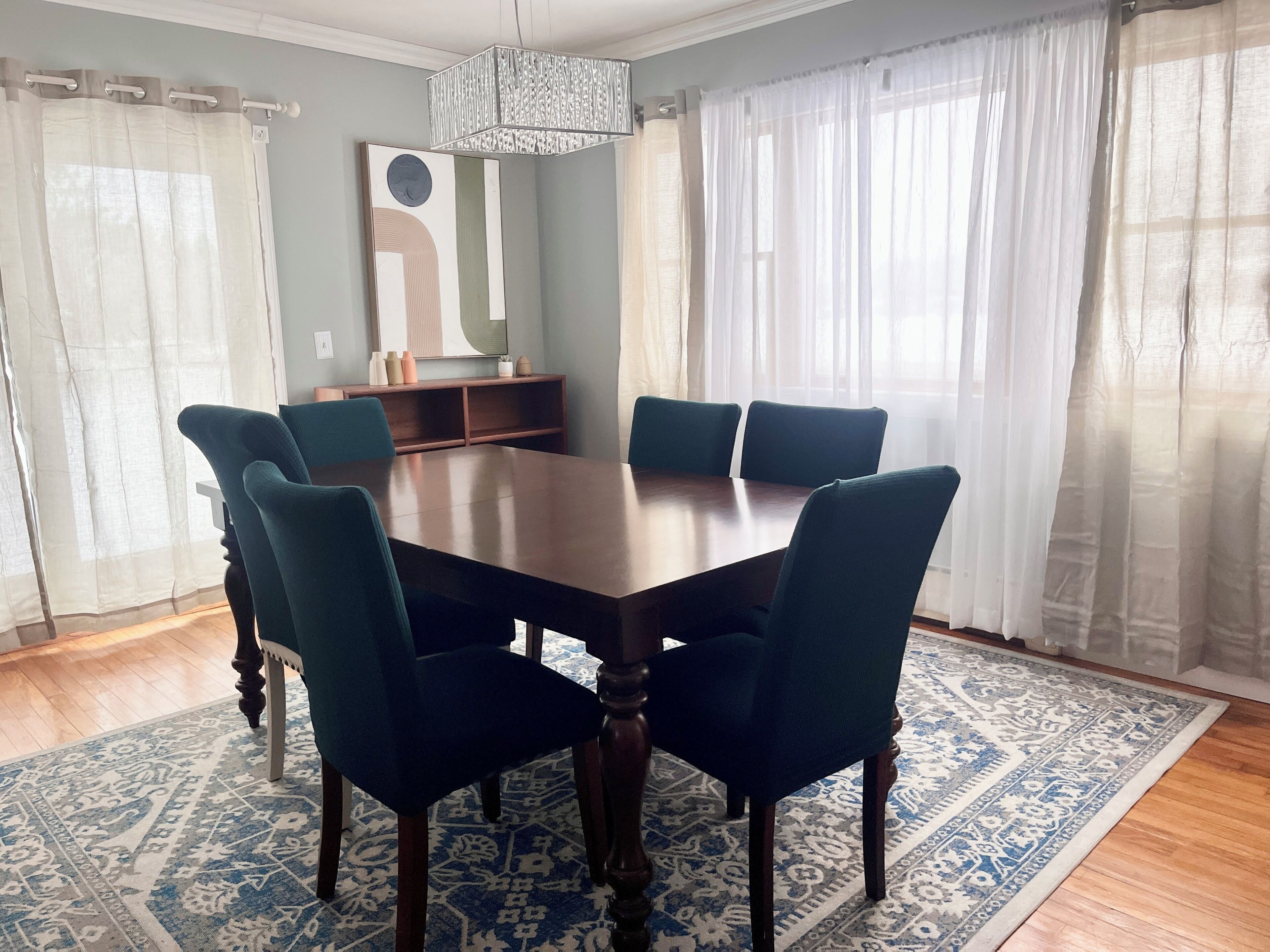 Une salle à manger avec une table rectangulaire entourée de six chaises, un tapis à motifs et un lustre.