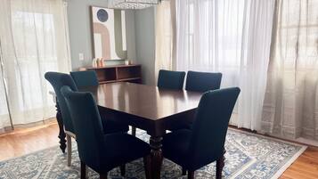 Une salle à manger avec une table rectangulaire entourée de six chaises, un tapis à motifs et un lustre.