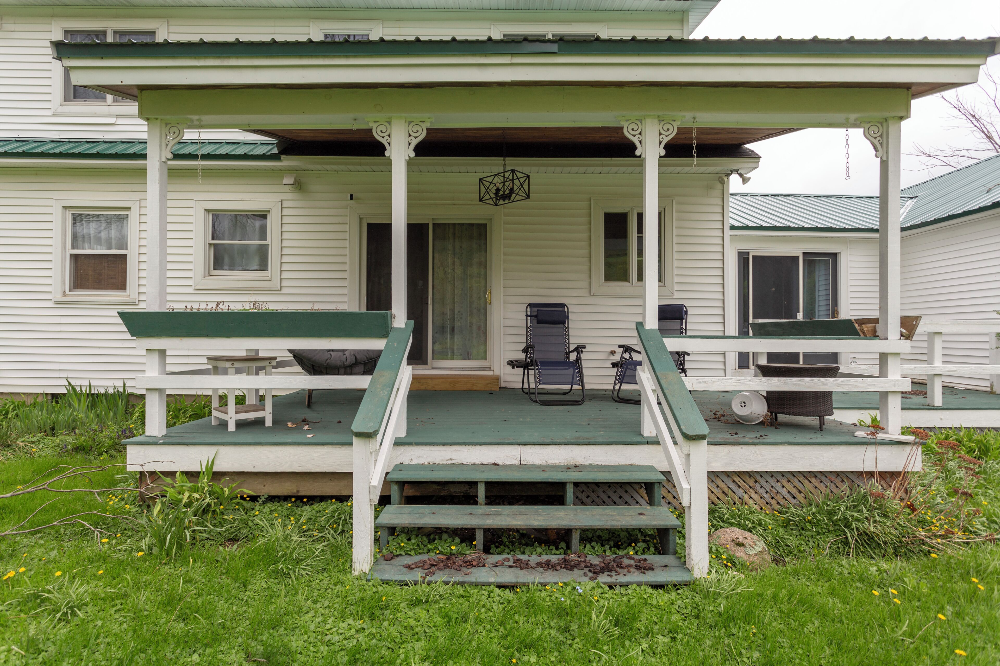 A porch with two chairs and a table, a door, and a small step leading up to the porch.