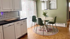 A kitchen with white cabinets, a dishwasher, a wooden cutting board, a round dining table with chairs, and a floral-patterned rug. - Gorgeous 5-bedroom house in welcoming Ellicottville perfect for families (Ellicottville)