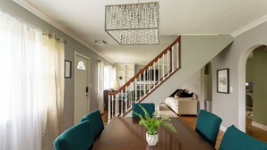 A dining room with a wooden table, teal chairs, a potted plant, a staircase, and a living area with a sofa and a coffee table. - Gorgeous 5-bedroom house in welcoming Ellicottville perfect for families (Ellicottville)