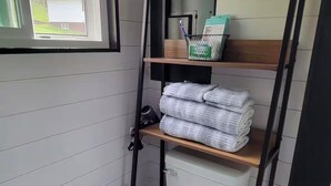 A compact bathroom with a toilet, a window, a shelf with towels, and a mirror. - Cozy 1-bedroom tiny house in beautiful Parkersburg,WV (Parkersburg)