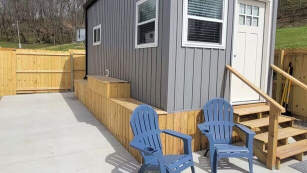A small, single-story building with a grey exterior and a wooden deck area. There are two blue chairs and a wooden staircase leading to a door. - Cozy 1-bedroom tiny house in beautiful Parkersburg,WV (Parkersburg)