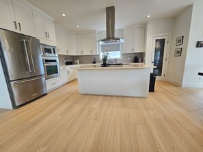A modern kitchen with stainless steel appliances, a central island, and light wood flooring. - Luxe 4BD family retreat w/AC, Yard, Bunks and King (Calgary)