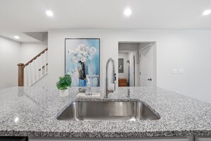 A kitchen with granite countertops, a stainless steel sink, a potted plant, and a painting on the wall. - Modern 3BR Townhome- Perfect for Short/Long Stays- Vacation or Traveling Pros! (Myrtle Beach)