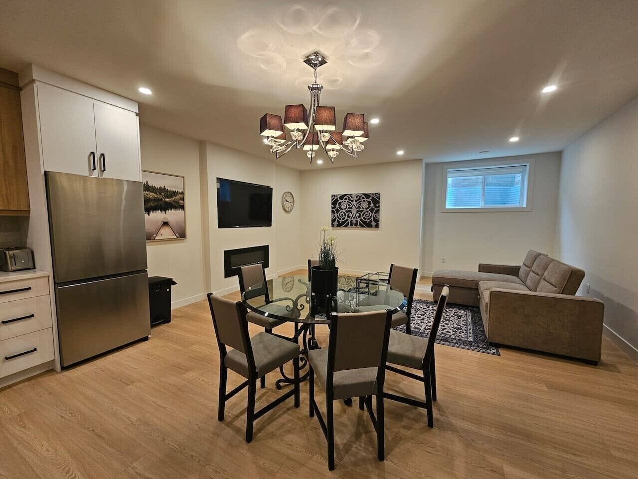 A modern kitchen with a built-in refrigerator, a dining table with chairs, a sofa, and a chandelier.