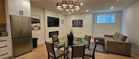 A modern kitchen with a built-in refrigerator, a dining table with chairs, a sofa, and a chandelier.