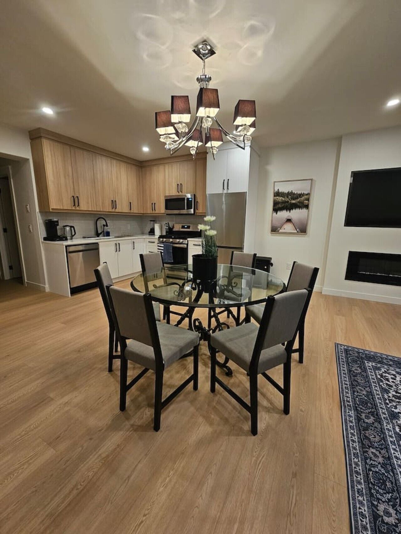 Una cocina moderna con armarios de madera, electrodomésticos de acero inoxidable y una mesa de comedor de vidrio con sillas.