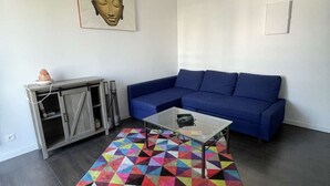 Ein Wohnzimmer mit einem blauen Sofa, einem Glastisch, einem farbenfrohen geometrischen Teppich, einem Schrank und einer Buddha-Statue.