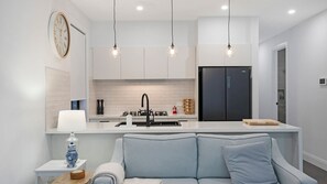 A modern kitchen with a black refrigerator, white cabinets, and pendant lighting. - Salt & Spa Norah Head (Norah Head)