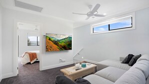 A modern living room with a flat-screen TV, a ceiling fan, a window with a view, a sofa, and a coffee table. - Salt & Spa Norah Head (Norah Head)