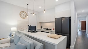 A modern kitchen with a central island, a black refrigerator, and a clock on the wall. - Salt & Spa Norah Head (Norah Head)