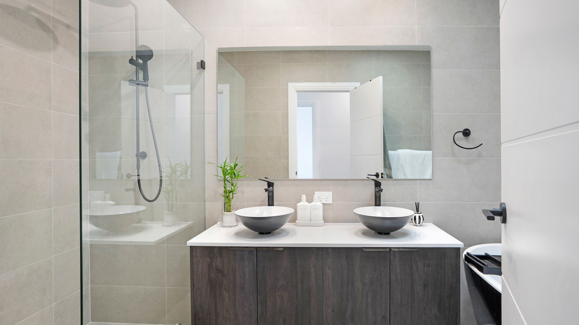 Een moderne badkamer met een douchecabine van glas, twee wasbakken met brede kommen, een spiegel boven de wasbakken en een houten kastje eronder.