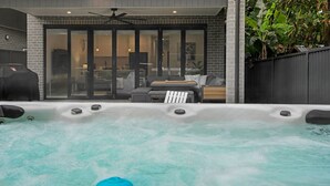 A hot tub with a patio area, a ceiling fan, and a brick wall. - Salt & Spa Norah Head (Norah Head)