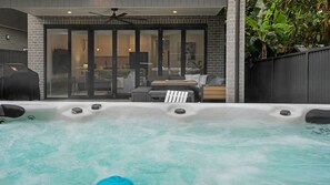 A hot tub with a patio area, a ceiling fan, and a brick wall. - Salt & Spa Norah Head (Norah Head)