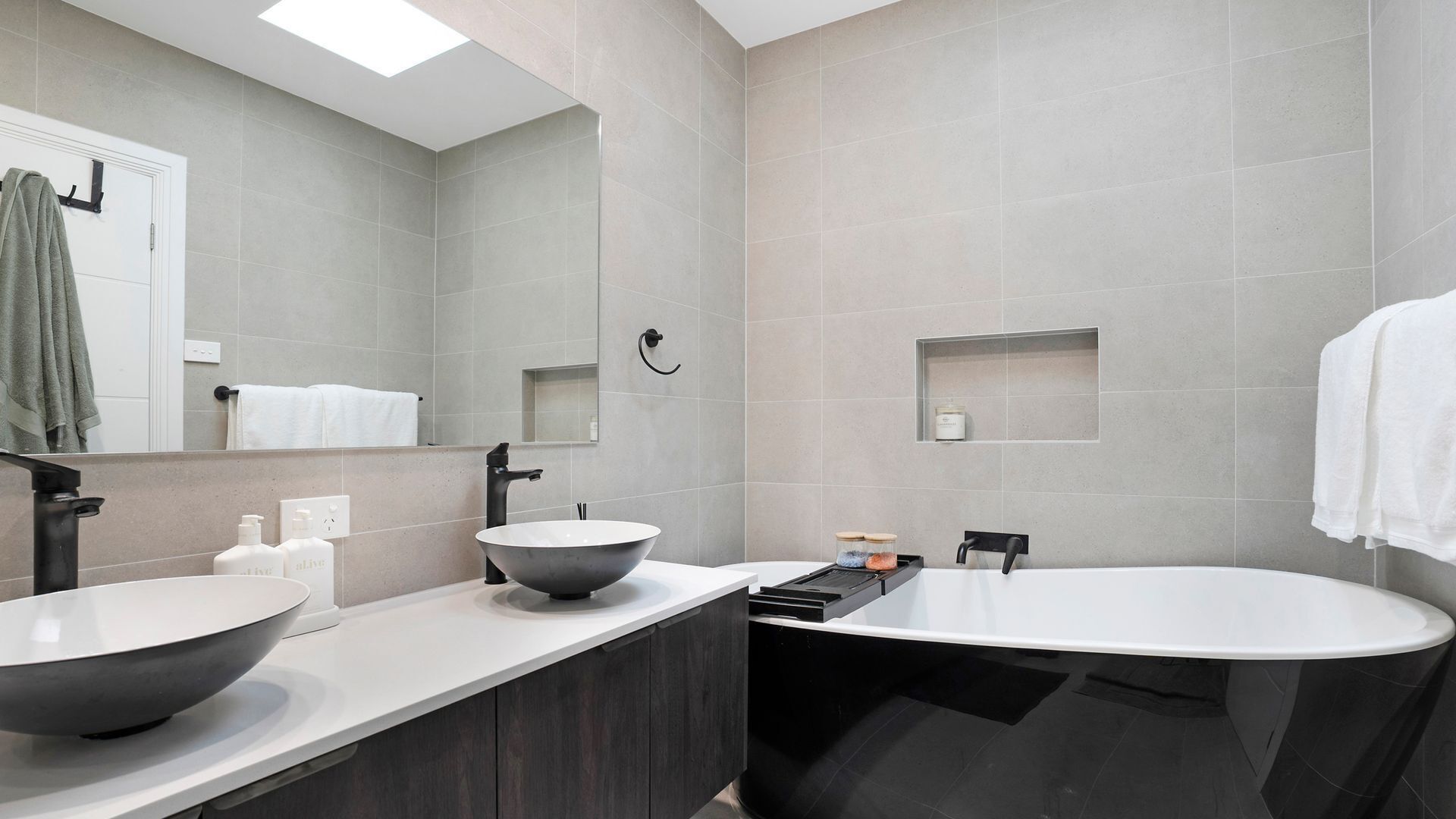 Een moderne badkamer met twee wastafels, een ruim bad en een spiegel.