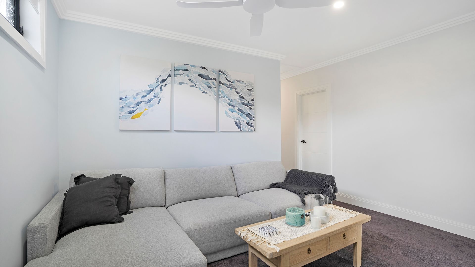 A modern living room with a grey sectional sofa, a wooden coffee table with decorative items, and abstract wall art.