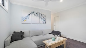 Un salon moderne avec un canapé d’angle gris, une table basse en bois agrémentée d’objets décoratifs et des œuvres d’art abstraites accrochées au mur.