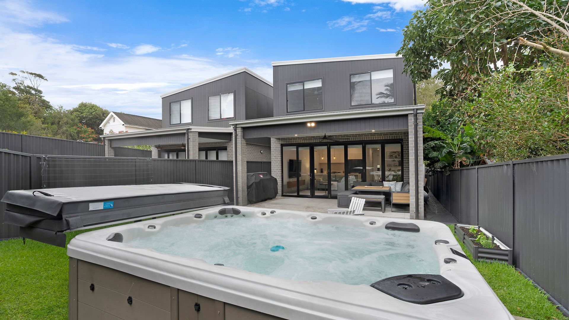 Une maison moderne dotée d’un jacuzzi, d’un espace salon extérieur et d’une terrasse couverte.