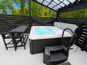 Jacuzzi con una silla, una mesa y un banco, todo bajo una zona cubierta con vistas a árboles.