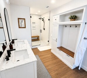 Un baño moderno con un espejo grande, dos lavamanos, una ducha y un vestidor.