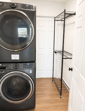Une buanderie équipée de machines à laver et de sèche-linge superposés, d’un étendoir métallique et d’une porte blanche.