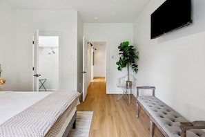 Un dormitorio con cama, un banco, una planta en maceta y un televisor en la pared.