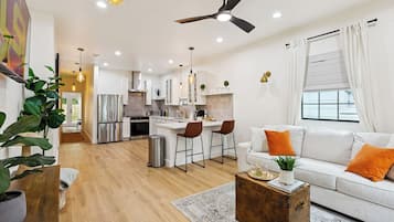 A modern kitchen with white cabinets, a stainless steel refrigerator, and a dining area with bar stools.